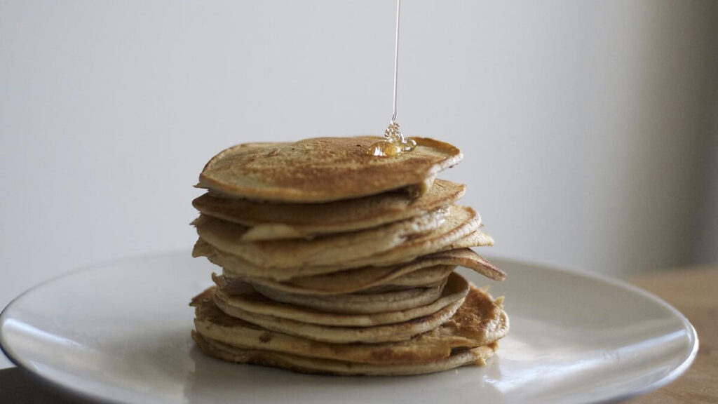 Xarope de açúcar sendo despejado sobre panquecas