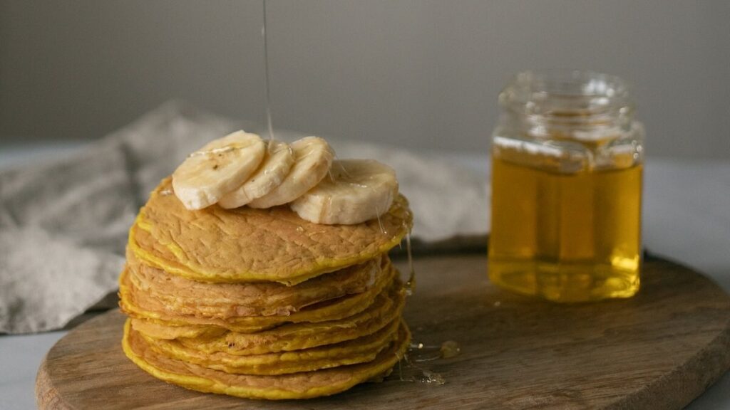 Xarope em panquecas doces, com banana sobre e vidro com xarope ao lado