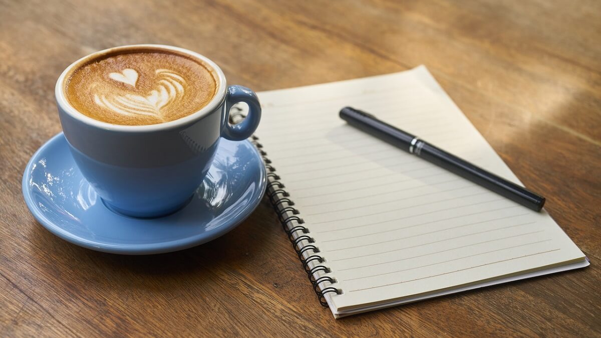 Xícara de cappuccino com caderno e caneta ao lado