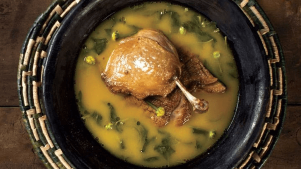 especie de sopa com liquido amarelado com folhas verdes, e um pedaço de carne de pato do tucupi